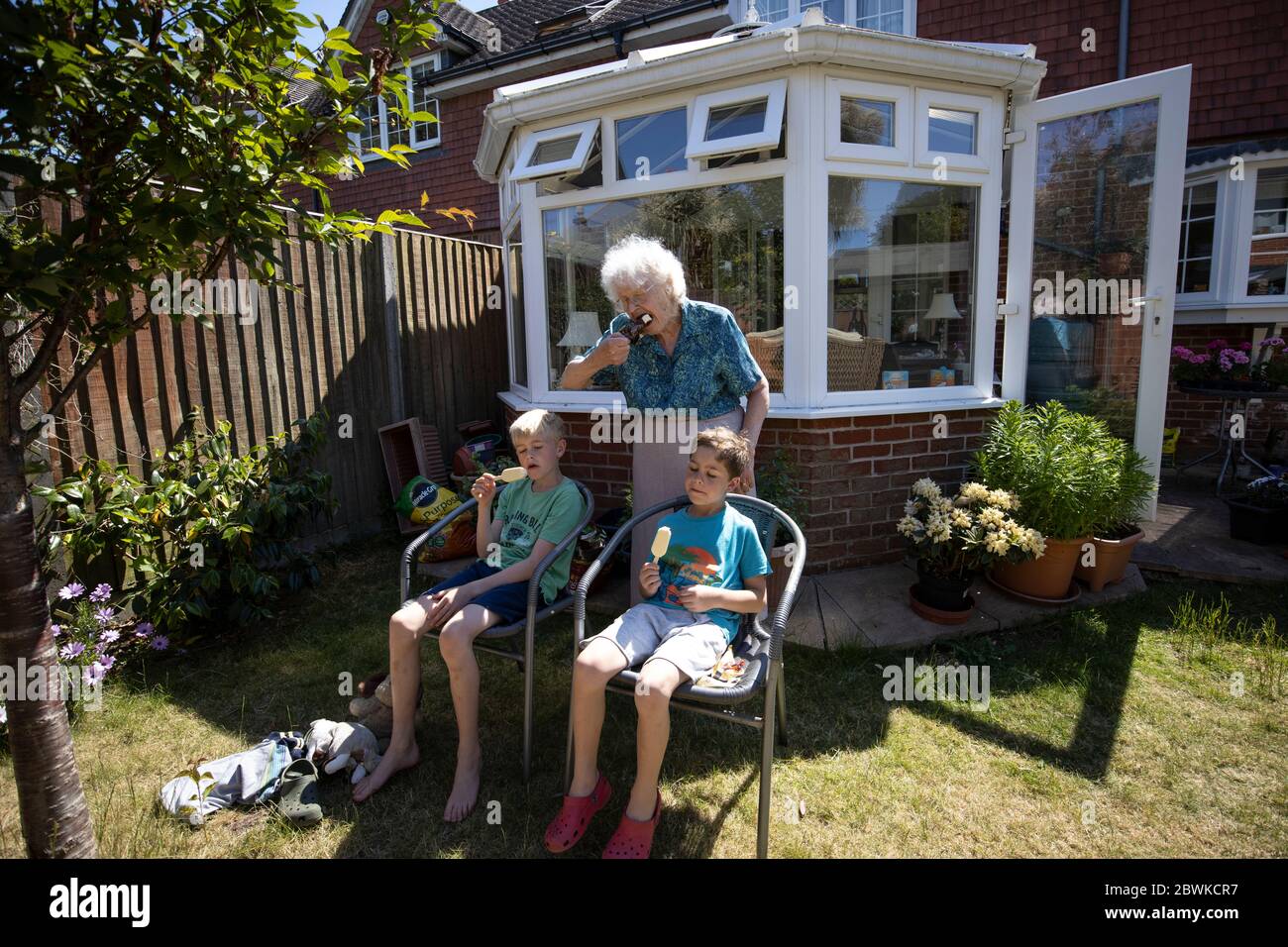 Femme âgée dans ses années 80, avec ses petits-fils appréciant le temps ensoleillé dans son jardin arrière, Angleterre, Royaume-Uni Banque D'Images