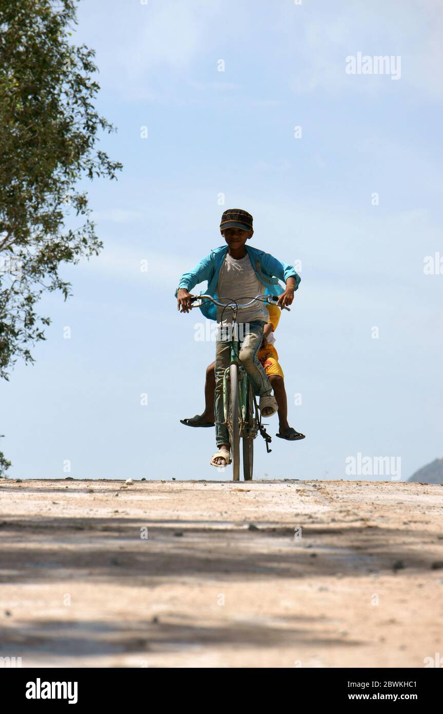 Garçon à vélo descendre la pente sur le chemin de la campagne déserte, deux enfants vietnamiens profiter de l'activité en plein air, vêtements sales, porter un chapeau, peau bronzée Banque D'Images