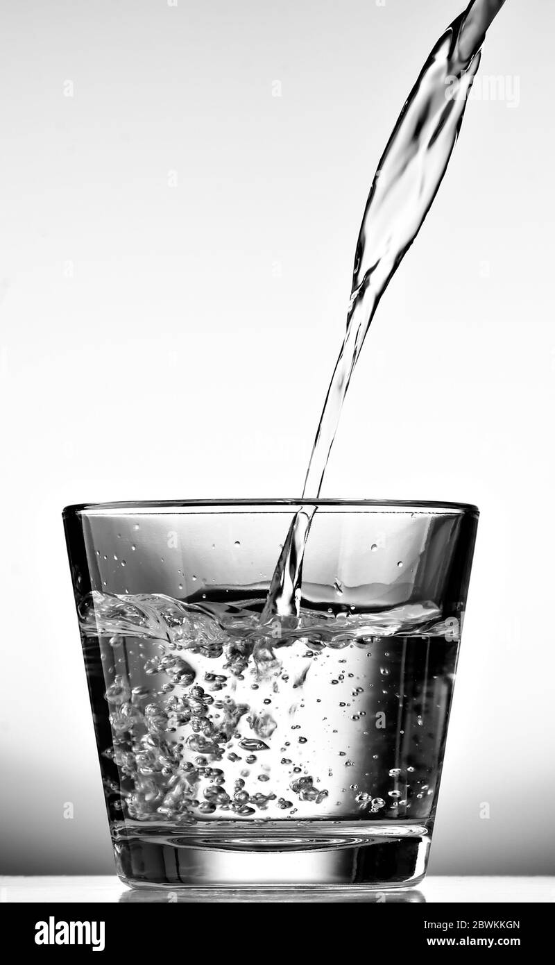 Verser de l'eau dans une tasse en verre sur fond blanc. Noir et blanc. Banque D'Images