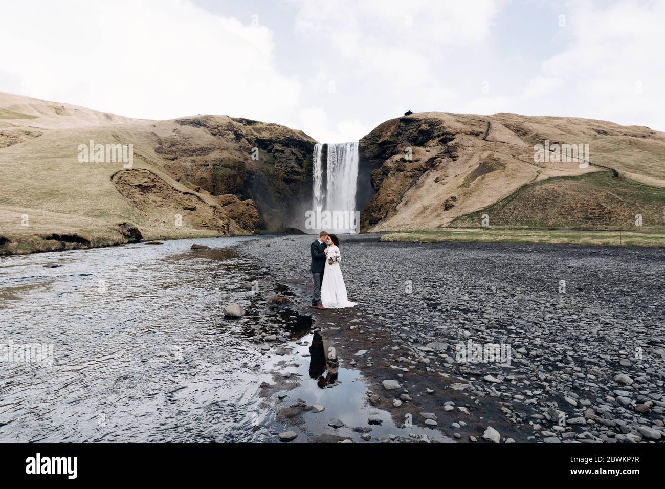 Destination mariage Islande. Couple de mariage près de la cascade de Skogafoss. La mariée et le marié s'embrasent près de la rivière. Banque D'Images