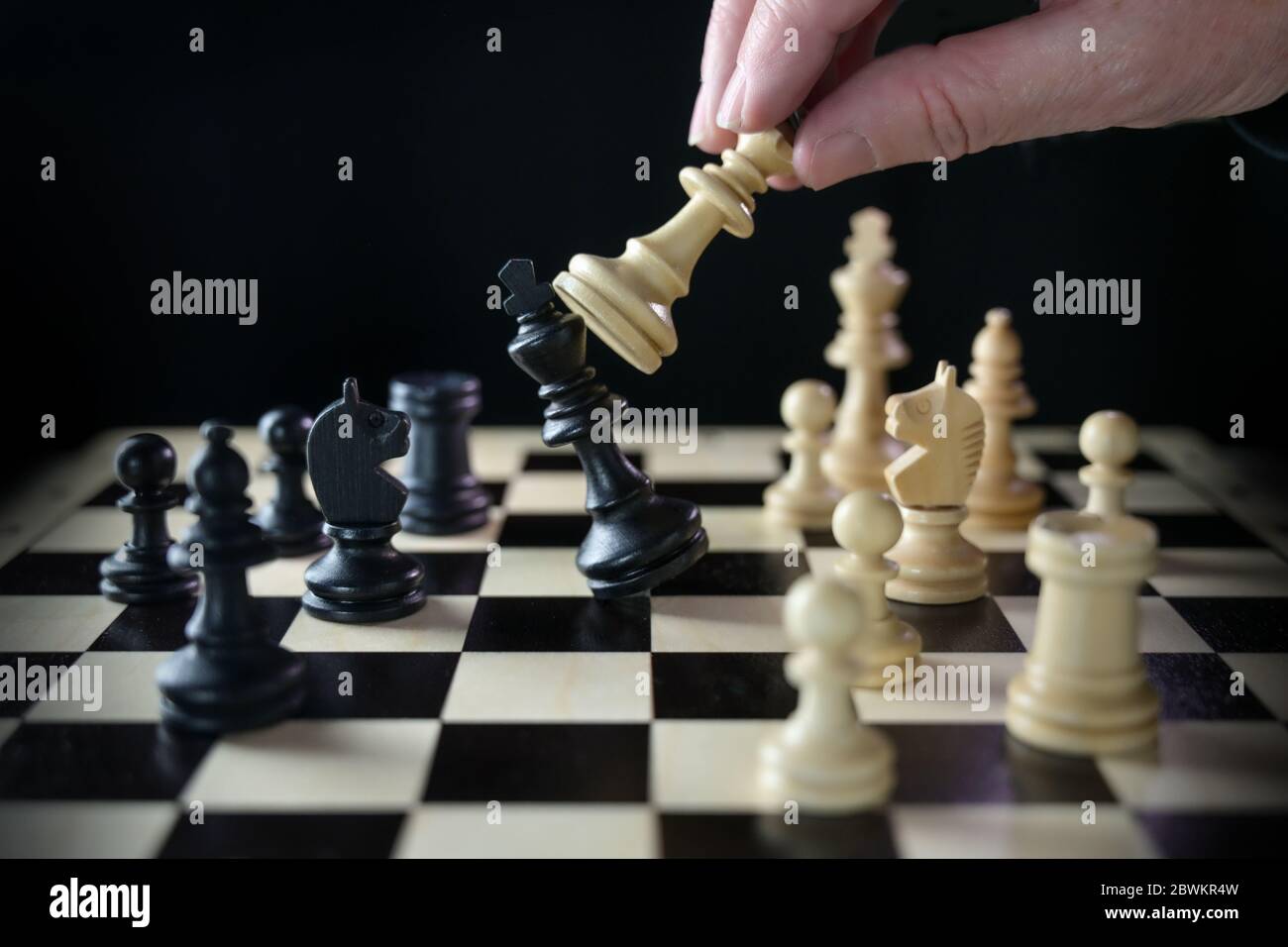 La main humaine joue aux échecs et bat le roi, le cochtier sur le chessboard contre un fond noir, un focus sélectionné, une profondeur de champ étroite Banque D'Images