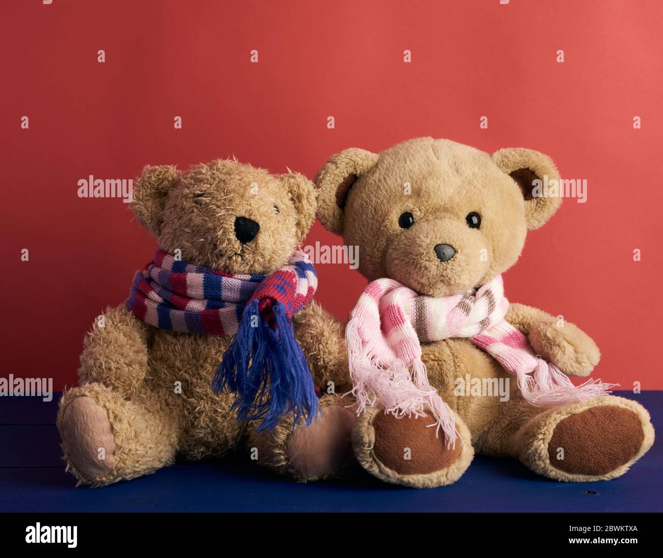 deux ours en peluche dans des foulards sont assis sur un fond rouge, gros plan Banque D'Images