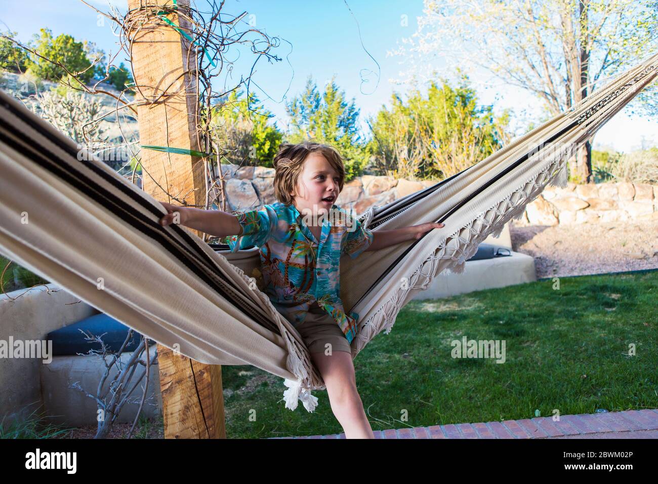 Un garçon de six ans balançant dans un hamac sur un patio à l'extérieur. Banque D'Images