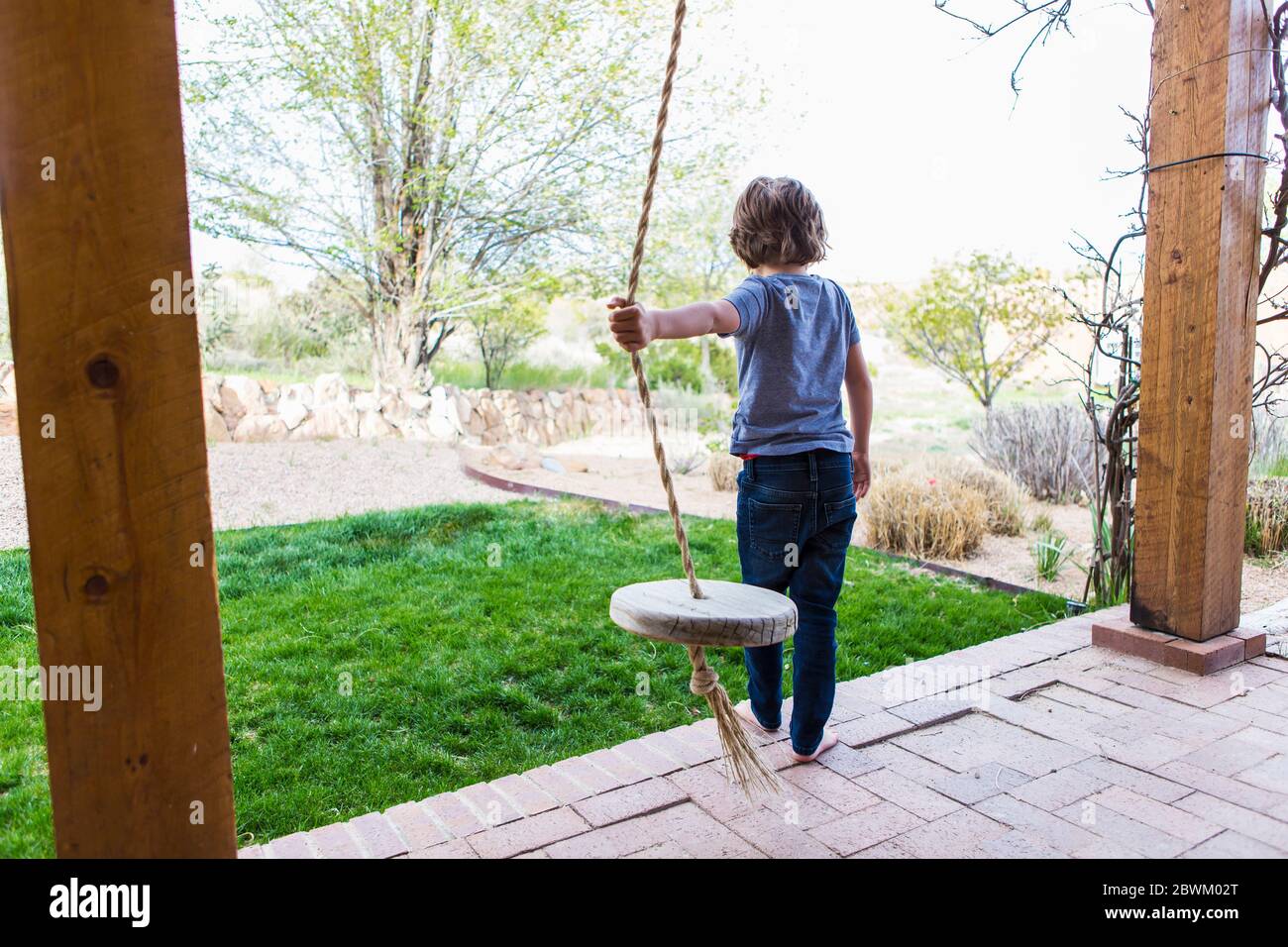 Garçon de six ans utilisant une corde balançoire sur un grand porche à l'ombre. Banque D'Images