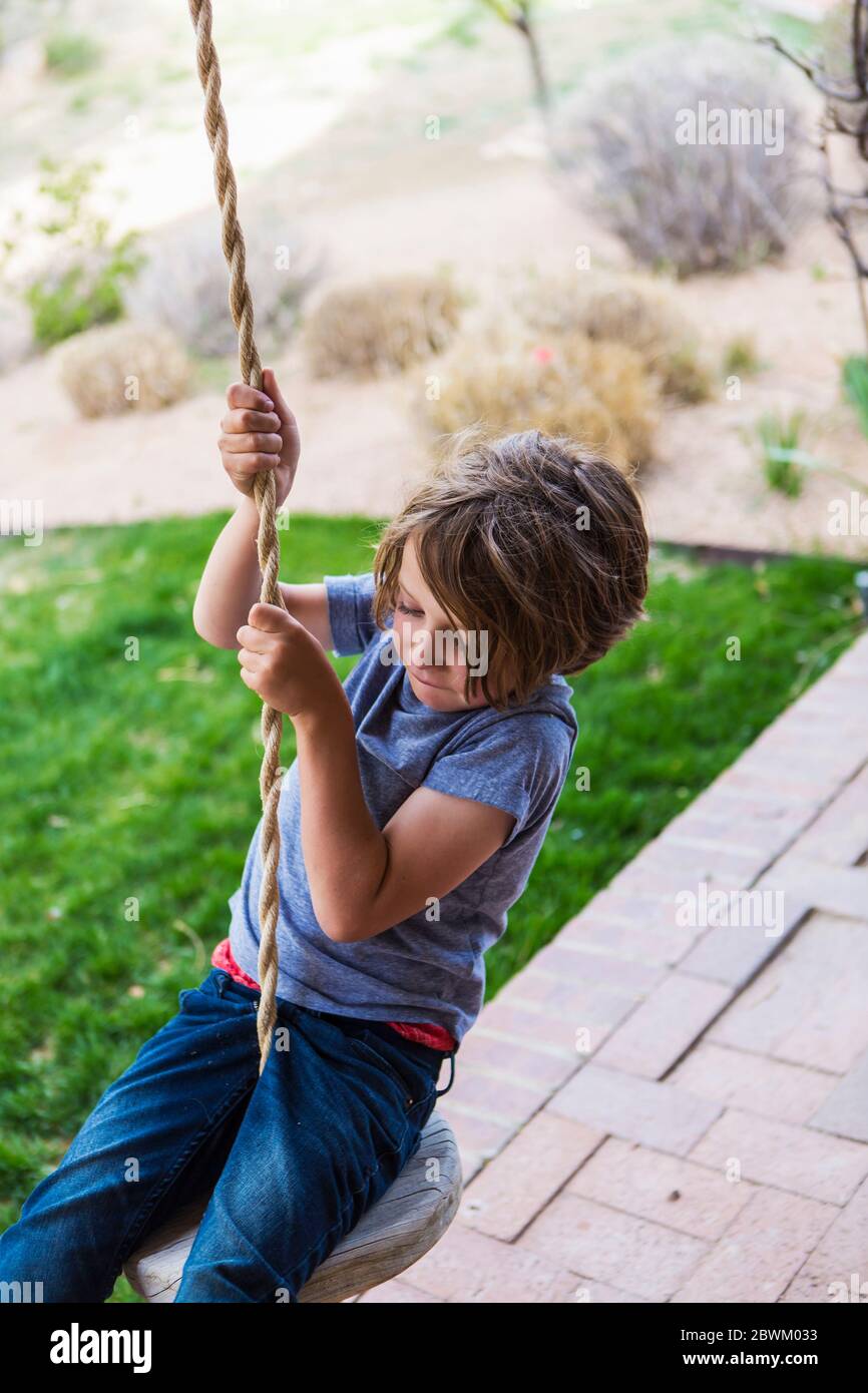 Garçon de six ans utilisant une corde balançoire sur un grand porche à l'ombre. Banque D'Images