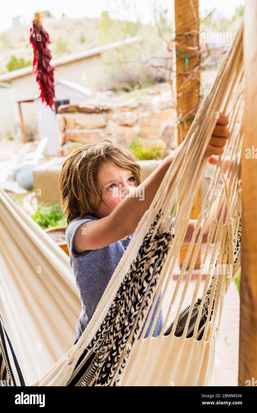 Garçon de six ans balançant dans un hamac sur une terrasse. Banque D'Images