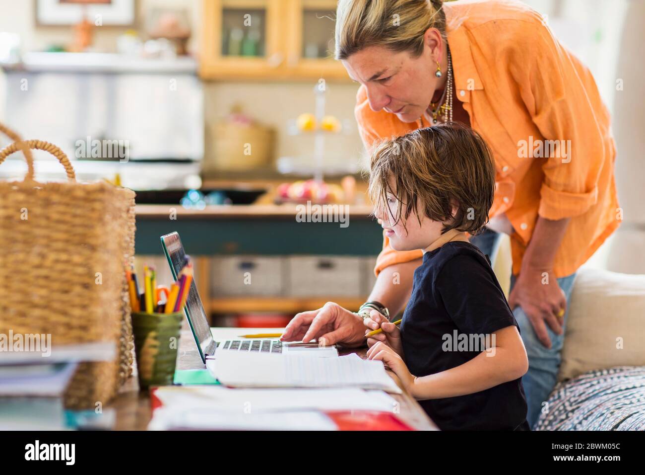 Femme adulte aidant son fils de six ans avec une session d'apprentissage à distance sur un ordinateur portable, à l'aide d'un pavé tactile. Banque D'Images