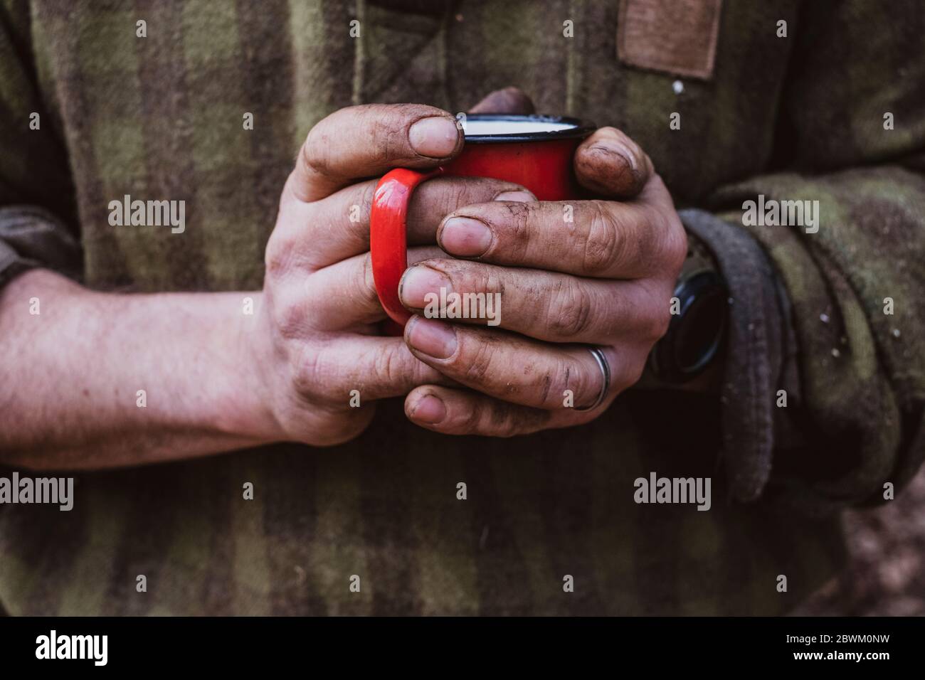 Gros plan d'un homme aux mains sales tenant une tasse en émail rouge. Banque D'Images