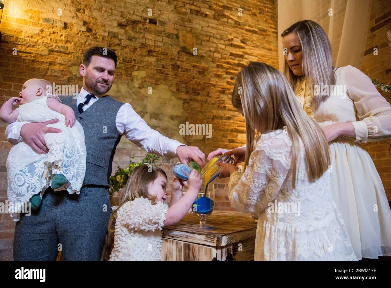 Famille versant du sable coloré dans un pot en verre lors de la cérémonie de dénomination dans une grange historique. Banque D'Images