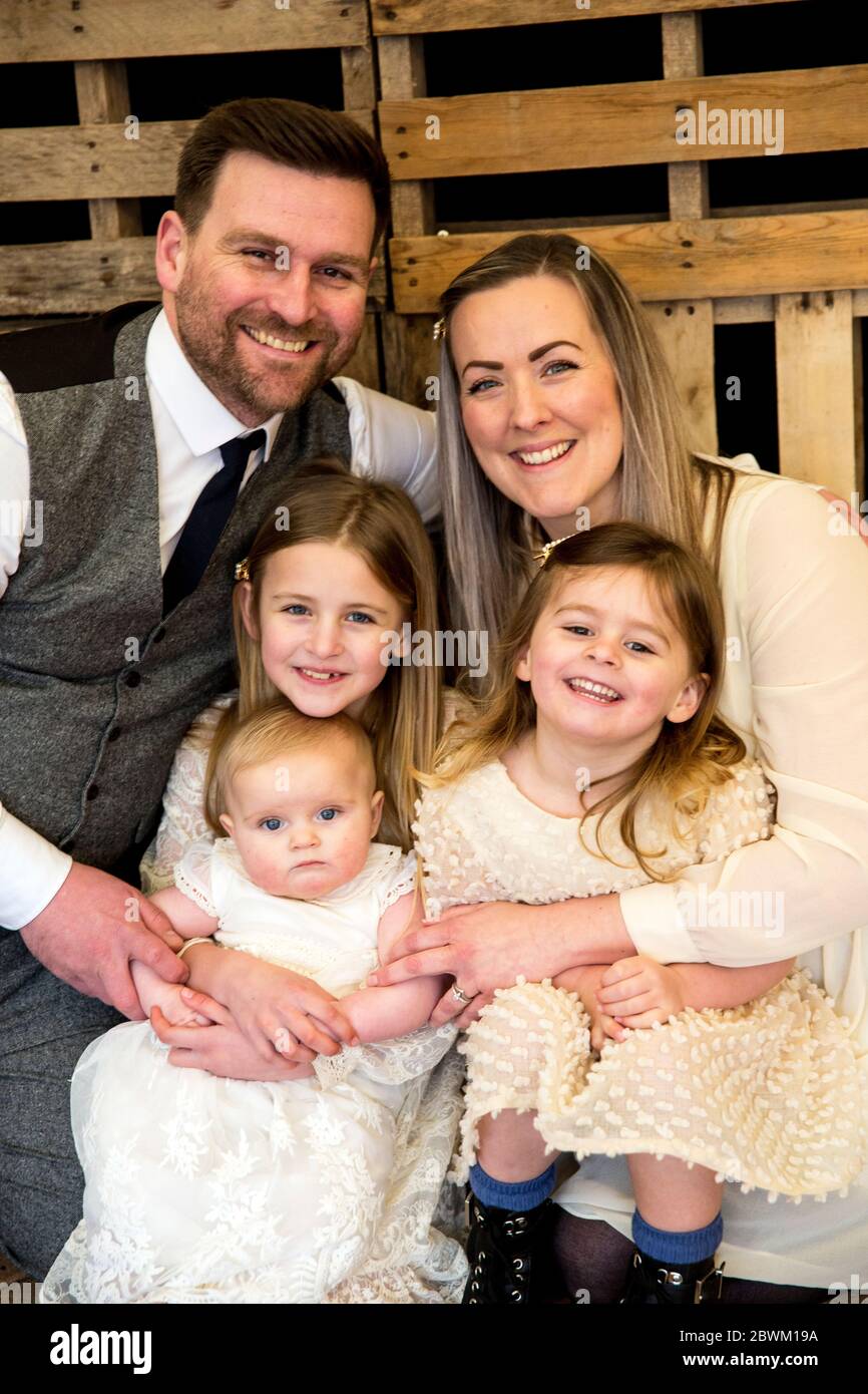 Portrait de parents souriants avec leurs trois jeunes filles lors de la cérémonie de dénomination dans une grange historique. Banque D'Images