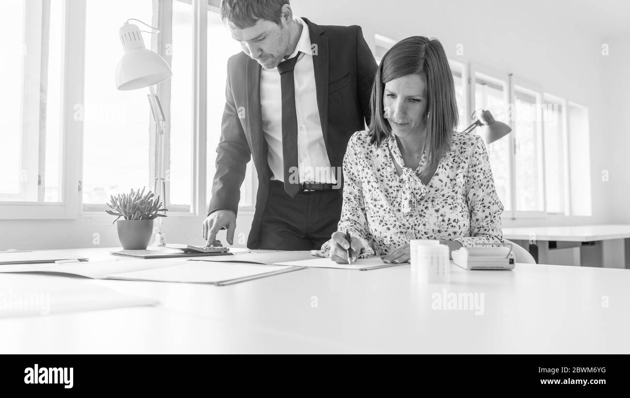 Deux partenaires d'affaires, un jeune homme et une femme, travaillant ensemble sur la paperasse à une grande table de bureau vu sous angle bas. Banque D'Images