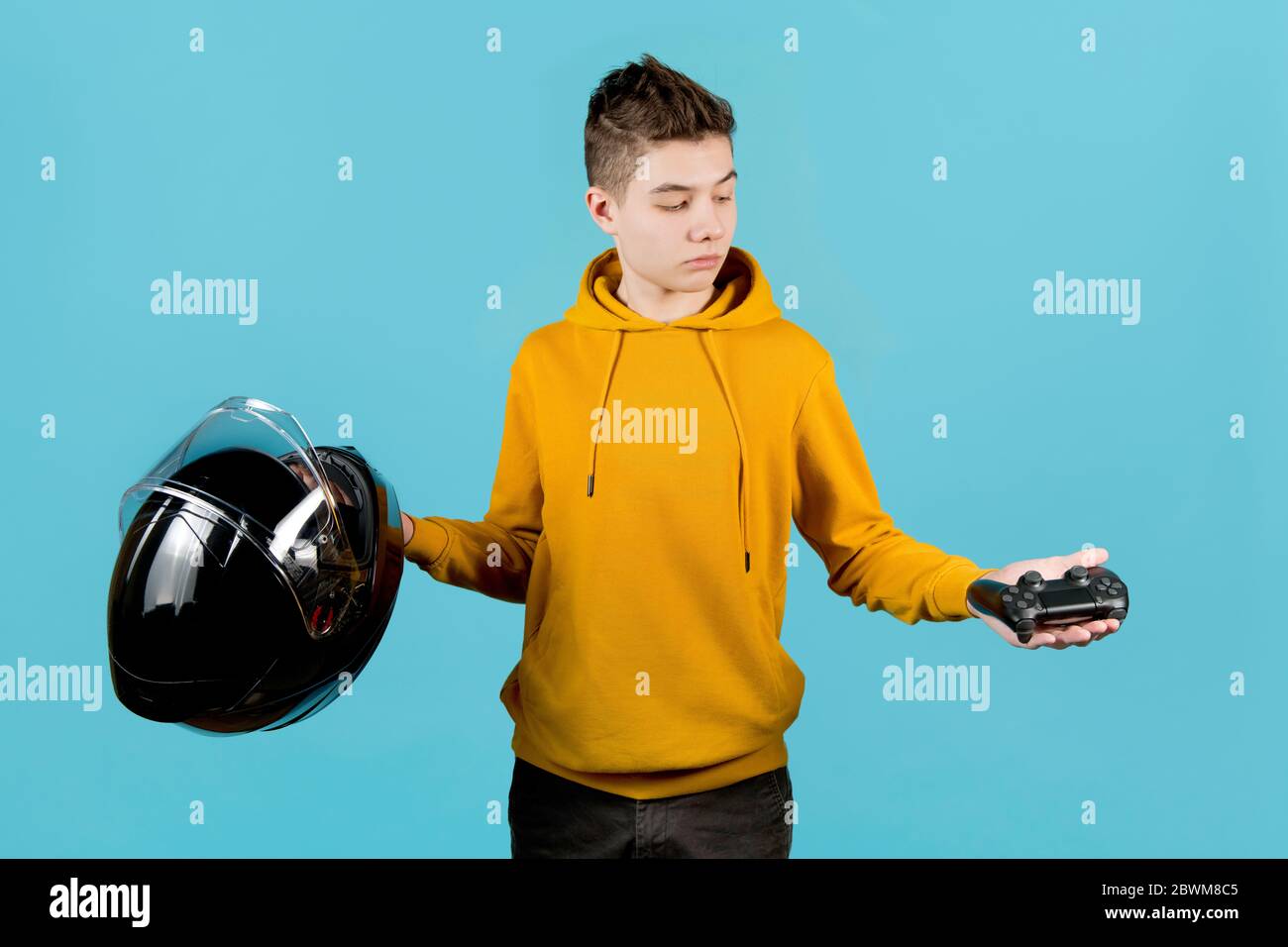 L'adolescent tient un joystick modifié sans marques d'identification et un casque de moto dans ses mains, en choisissant un joystick. Le choix entre réel Banque D'Images