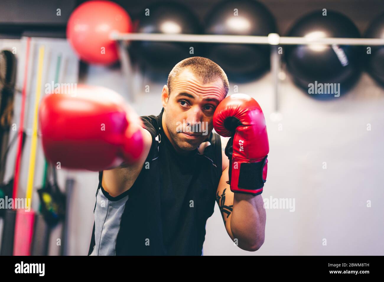 Boxeur latin avec gants rouges le jetant directement de la droite à l'intérieur d'une salle de gym. Concept de combat Banque D'Images