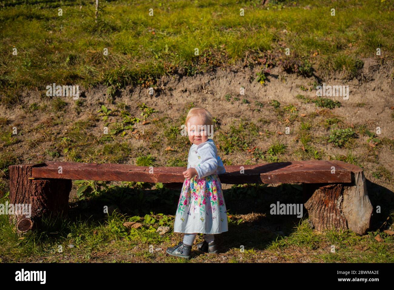 Un enfant d'un an, marchant sur l'herbe, en robe, en automne, un jour ensoleillé, souriant Banque D'Images