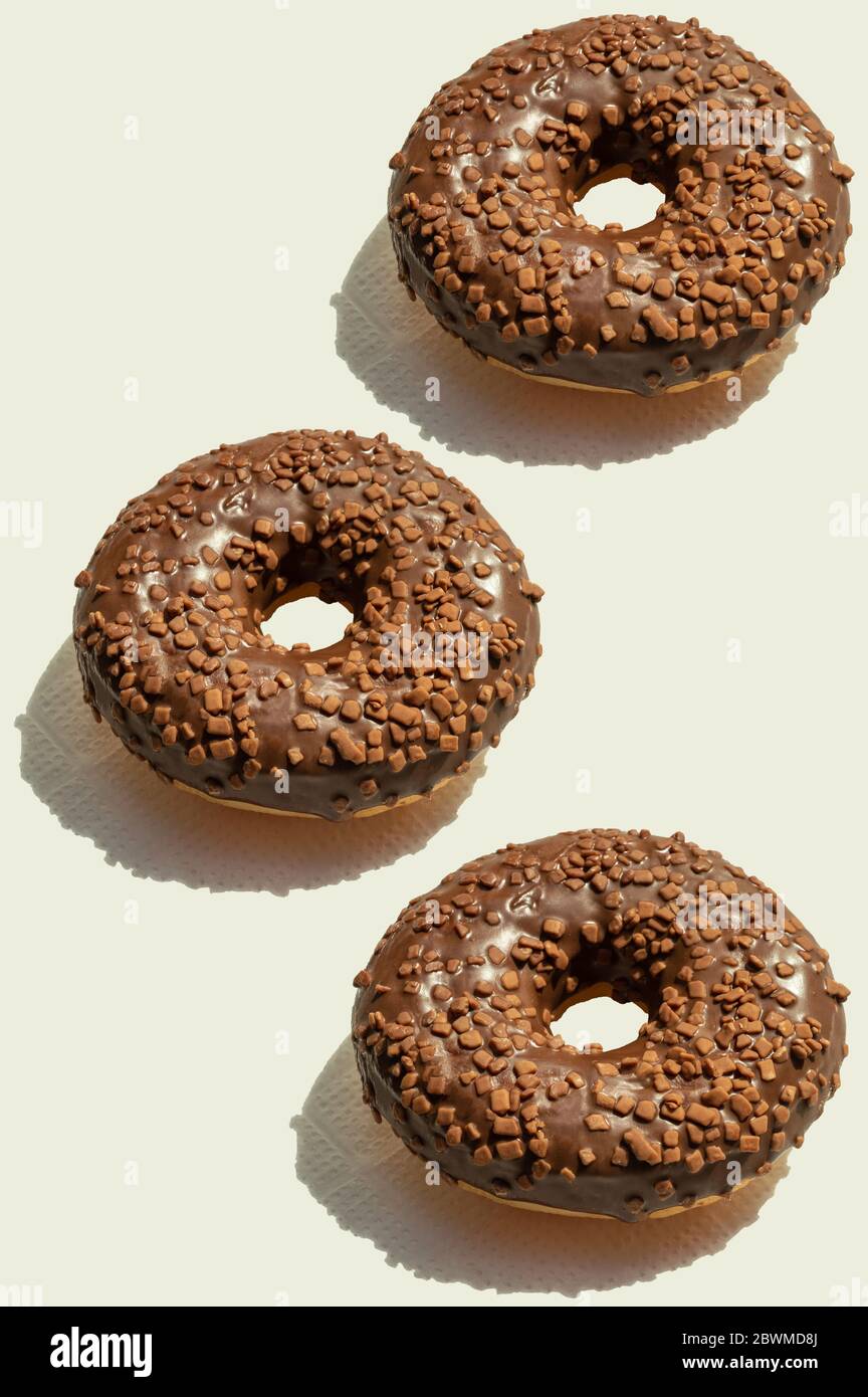 Trois donats au chocolat avec des ombres ensoleillées sur fond vertical. Desserts frais et délicieux. Modèle de nourriture créatif, vue du dessus. Géométrique tendance Banque D'Images