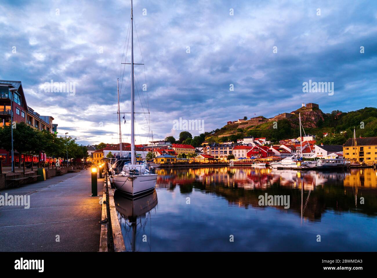 Halden, Norvège. Vue sur les maisons et yachts illuminés avec forteresse de Fredriksted en arrière-plan à Halden, Norvège, le soir avec soleil nuageux Banque D'Images