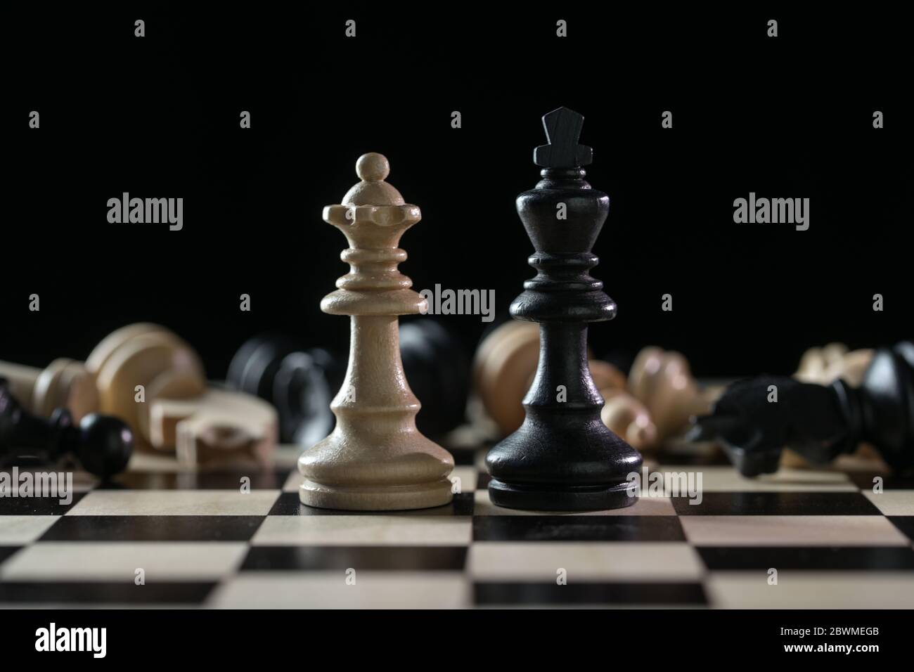Pièces d'échecs reine et roi devant un des échiquier tombés après un champ de bataille sur un échiquier sur fond noir, concept d'abus de pouvoir Banque D'Images
