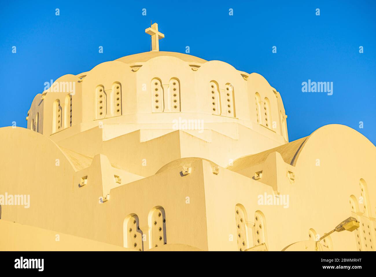 Détail de la cathédrale métropolitaine orthodoxe de Thira, sur l'île grecque de Santorin, au coucher du soleil créant une lueur jaune sur le bâtiment blanc Banque D'Images