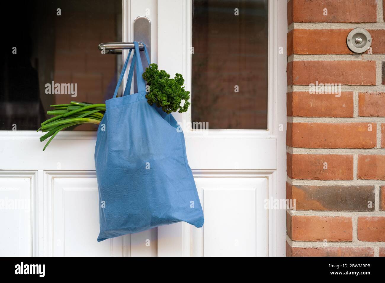 Le sac à provisions bleu avec des légumes frais et des produits a été accroché à la porte d'entrée, concept d'aide pendant la période de quarantaine en raison de l'infection par le coronavirus, Banque D'Images