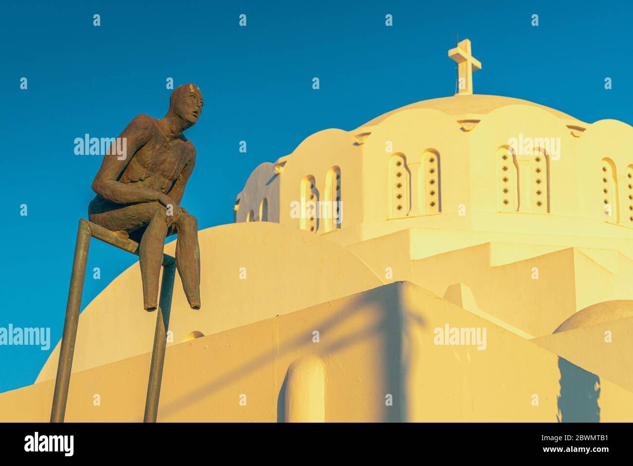 Un Sulpture moderne contre la cathédrale métropolitaine orthodoxe de Thira, Santorin, avec la lueur dorée du coucher du soleil Banque D'Images