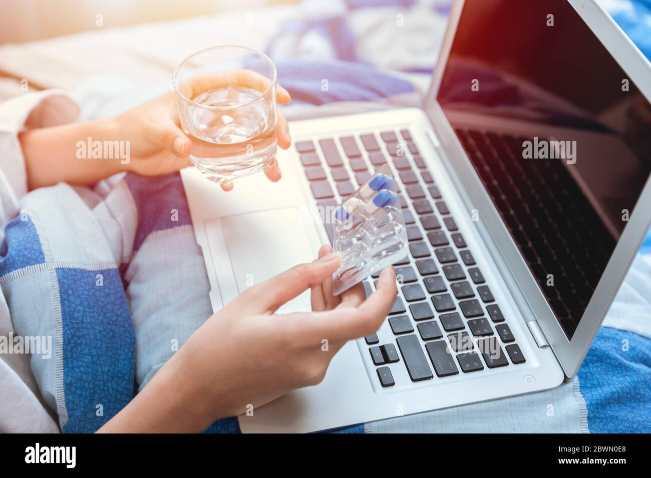 Les gens prennent une pilule pour le temps de médicament pendant le travail à la maison avec ordinateur portable tout en restant au lit. Banque D'Images