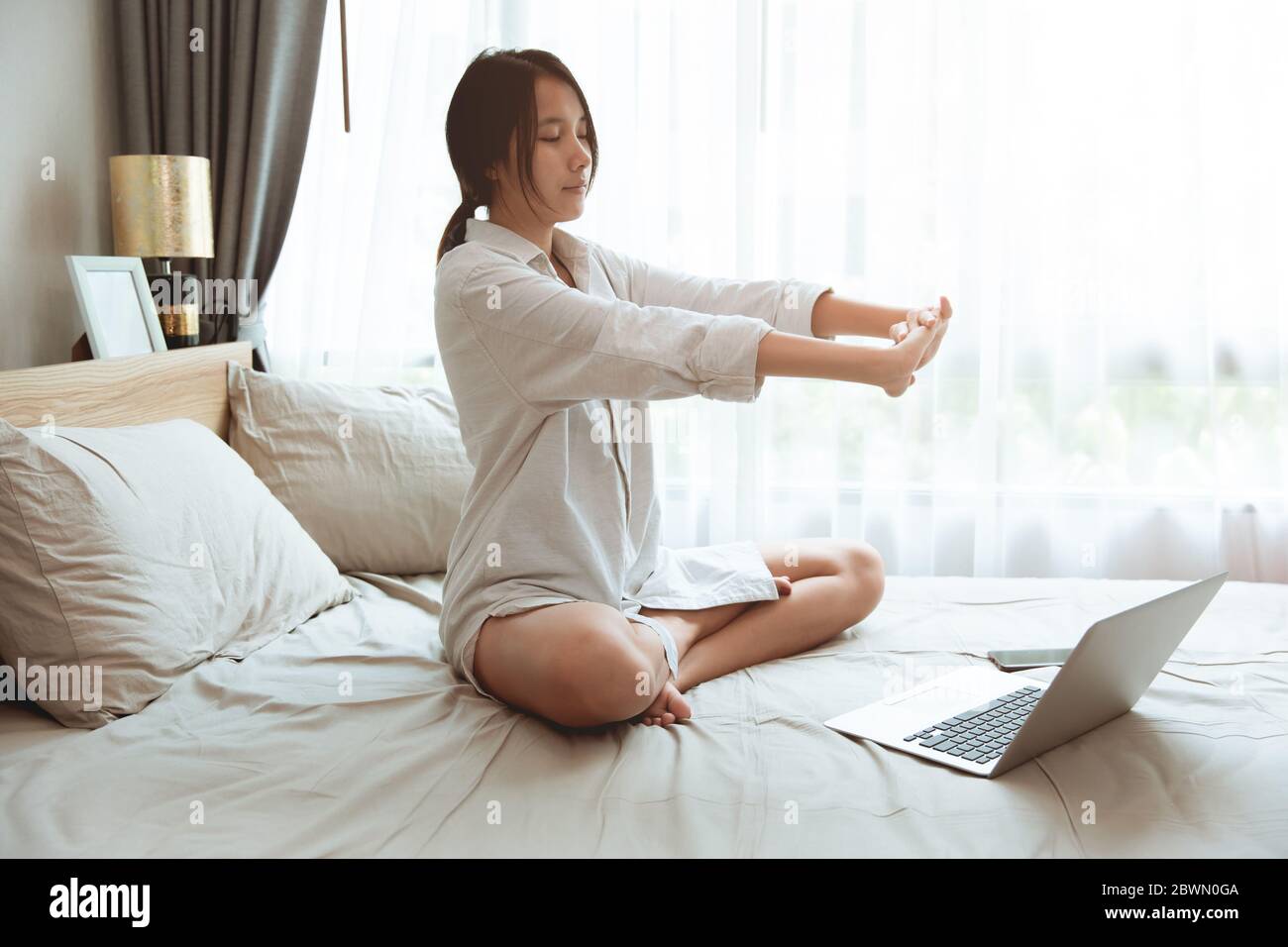 Jeune fille asiatique se réveiller le matin s'étirant travailler en ligne à la maison avec un ordinateur portable. Banque D'Images