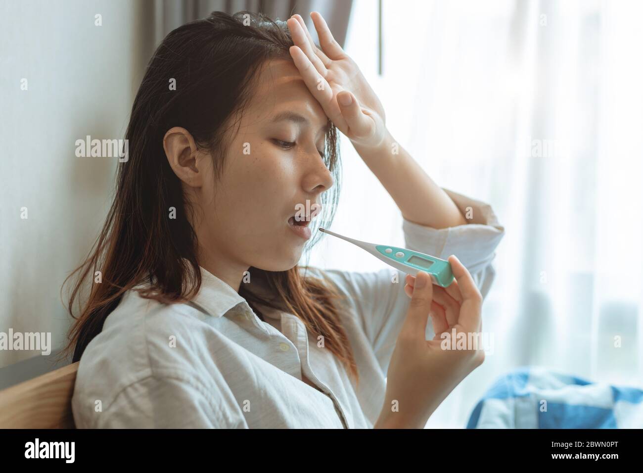 Les femmes asiatiques utilisant un thermomètre à test oral prennent la température corporelle pour diagnostiquer la grippe d'une infection à coronavirus. Banque D'Images