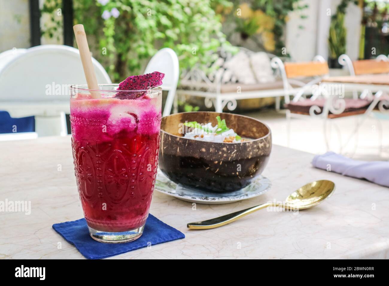 Jus rose avec pommes, betteraves, fruits de dragon et lime dans un verre avec paille de bambou et bol à smoothie sur la table du café Banque D'Images