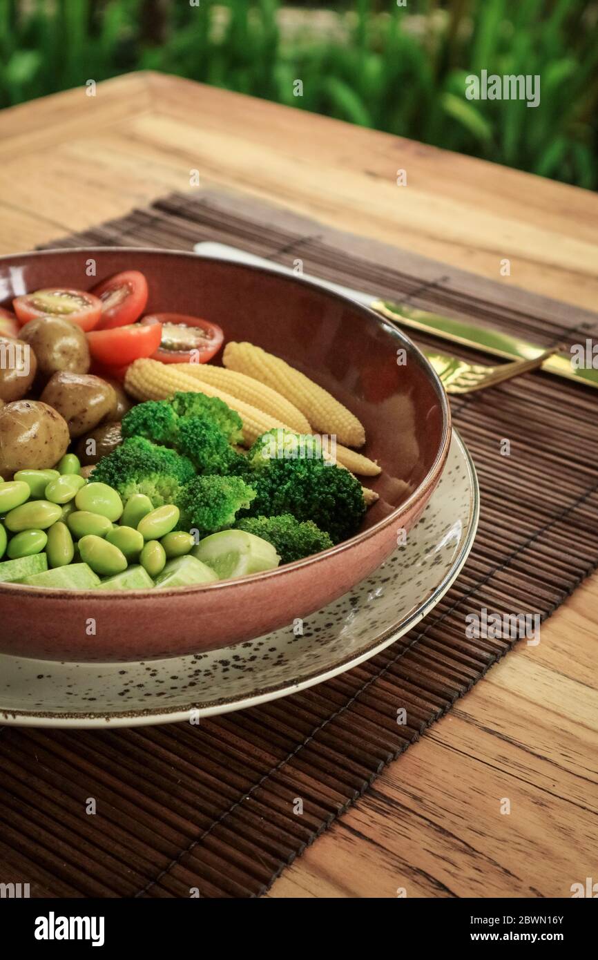 Coupe de Bouddha végétalien avec haricots edamame, tomates cerises, concombre, pommes de terre pour bébés, maïs, tofu sur table Banque D'Images