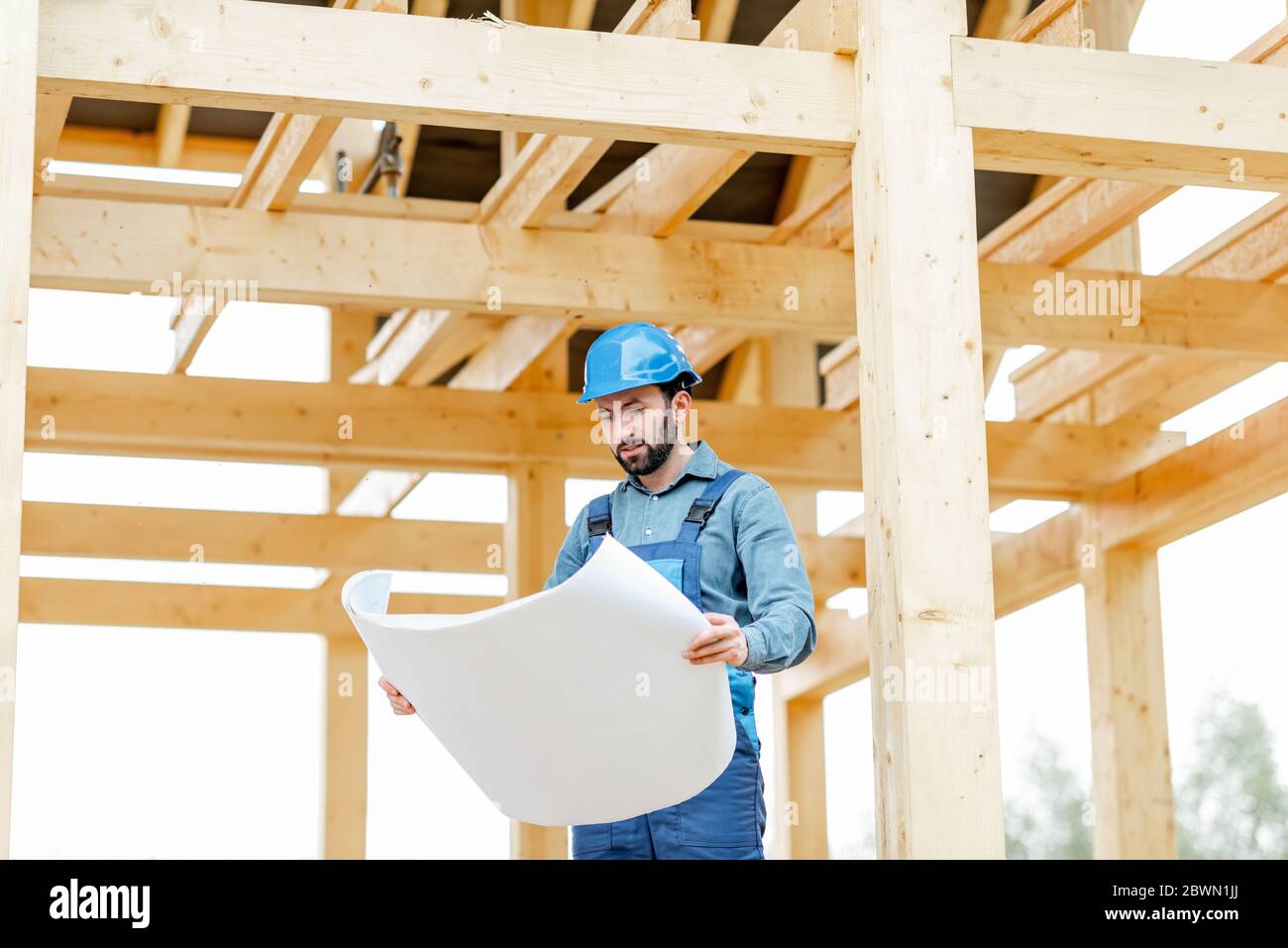 Builder en combinaison bleue et casque de chantier avec des plans sur le chantier. Construction en bois cadre maison concept Banque D'Images