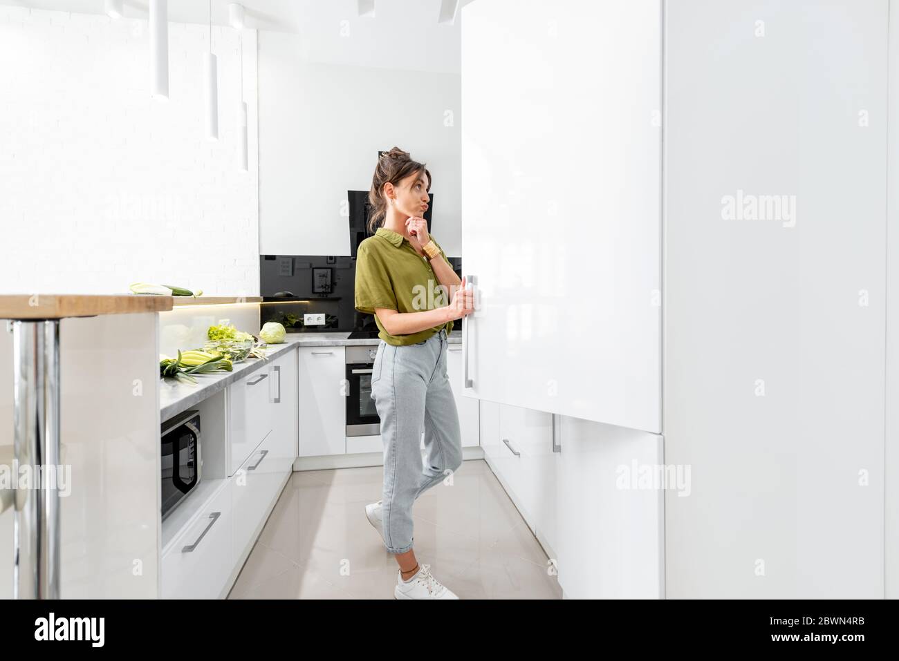 Femme cuisant des aliments sains dans la cuisine moderne à la maison, donnant sur le réfrigérateur, vue panoramique Banque D'Images