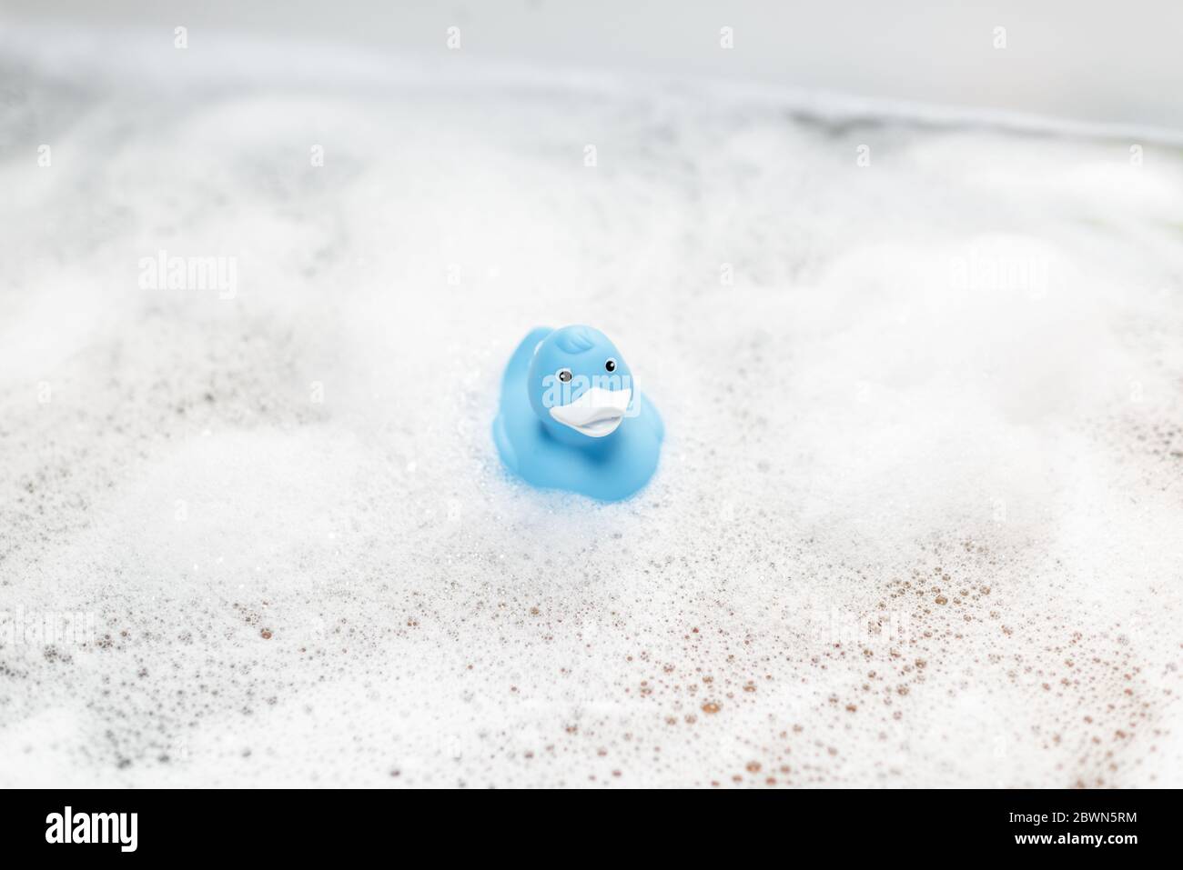 Canard en caoutchouc bleu nageant dans la baignoire avec mousse Banque D'Images