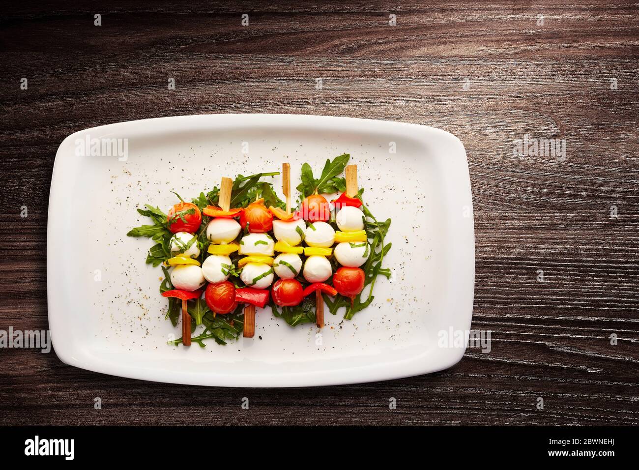 Directement au-dessus d'une dose de brochettes de tomates, de poivrons et de mozzarella sur un lit de roquette habillée servi dans une assiette Banque D'Images