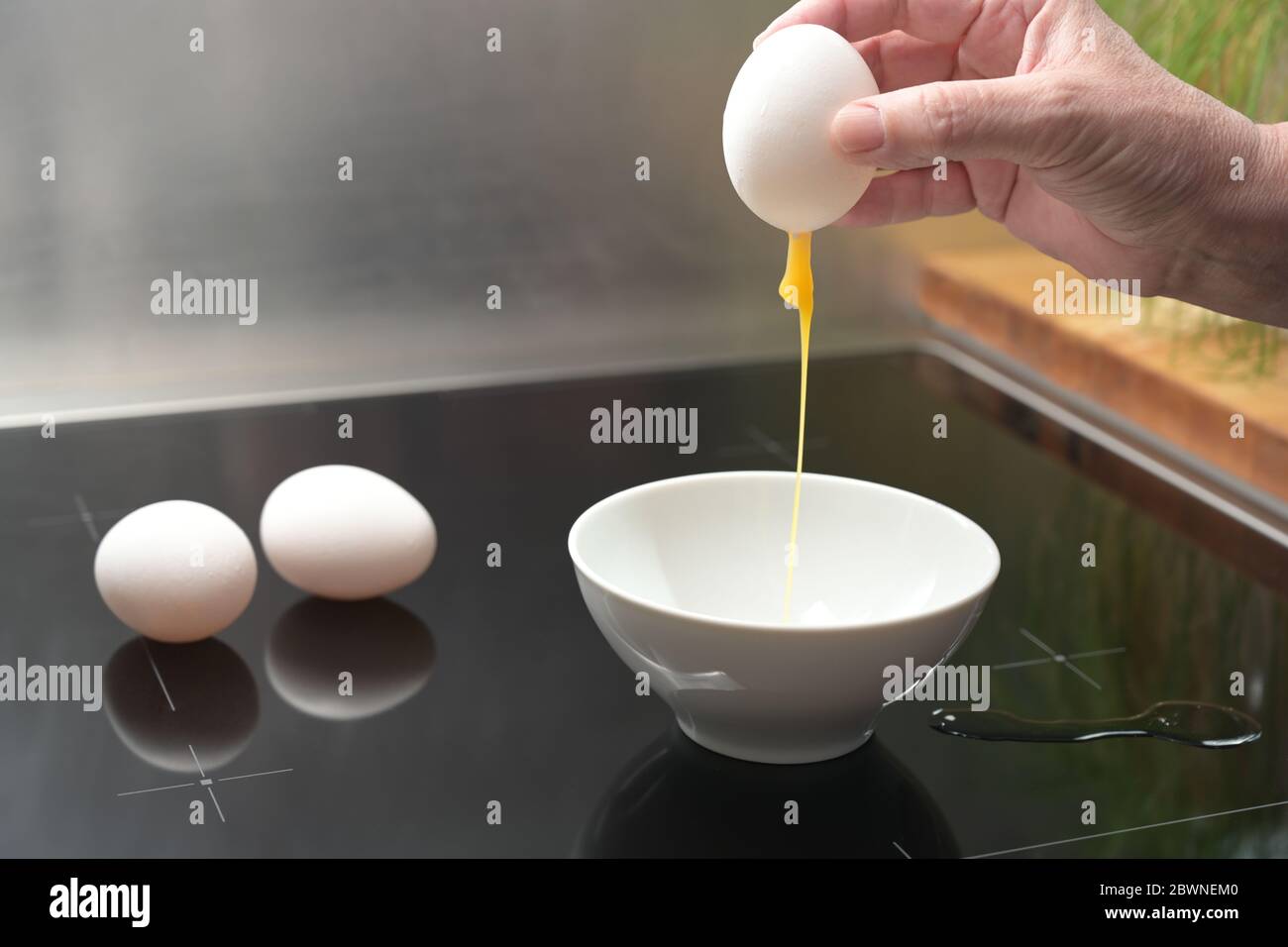 Main tient une coquille d'œuf entier avec le jaune qui fuit au-dessus d'un bol blanc, préparation pour la décoration de Pâques, espace de copie, foyer sélectionné, profondeur étroite de Banque D'Images