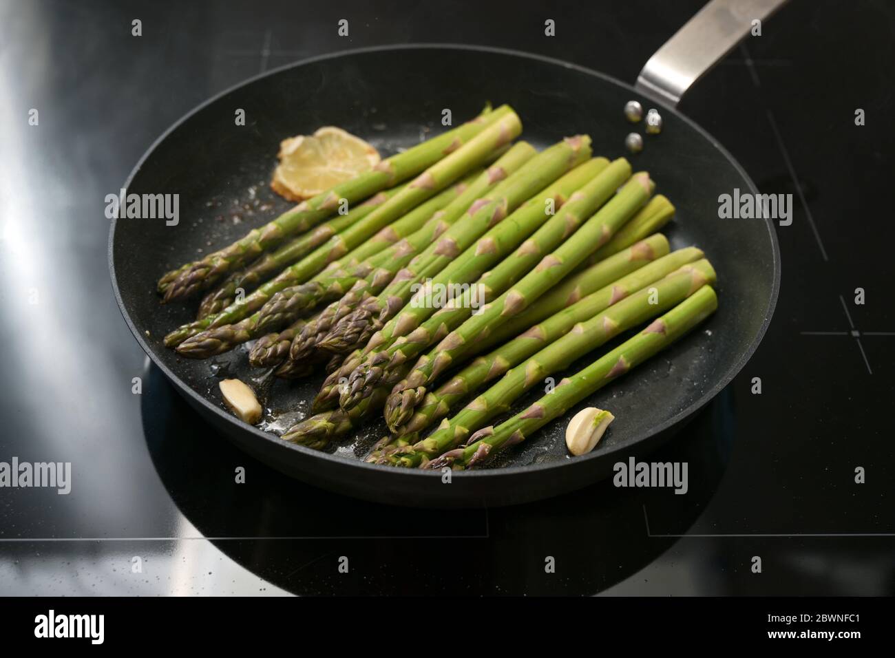 Faire frire des asperges vertes dans une poêle à l'ail et au citron sur une poêle noire, concept de cuisine saine pour un dîner de vacances, sélection de foyer, étroite d Banque D'Images