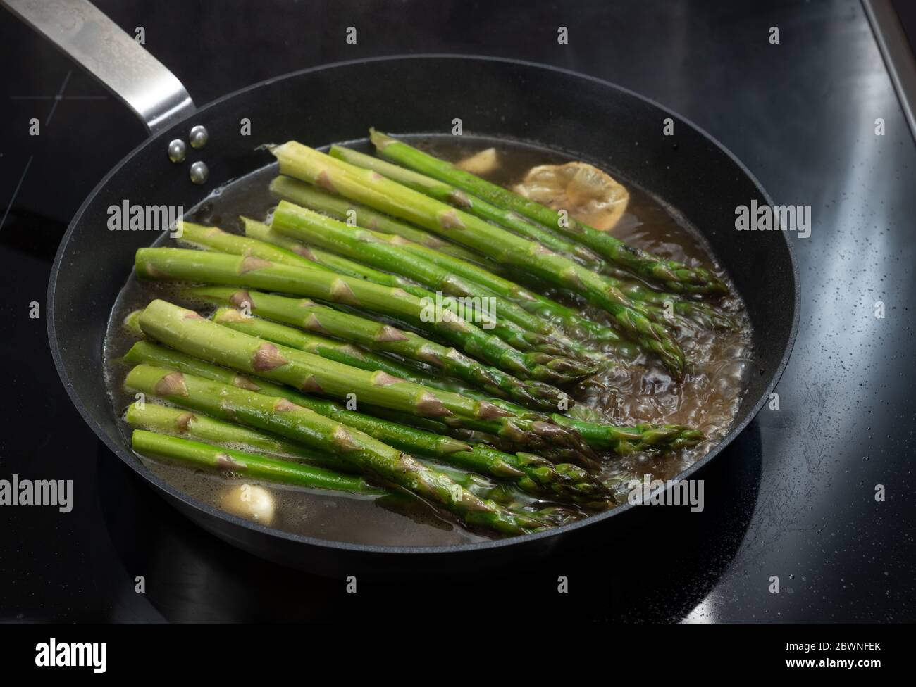 Cuisiner des asperges vertes biologiques dans une poêle sur un poêle noir pour un dîner végétarien sain, concentration sélectionnée, profondeur de champ étroite Banque D'Images