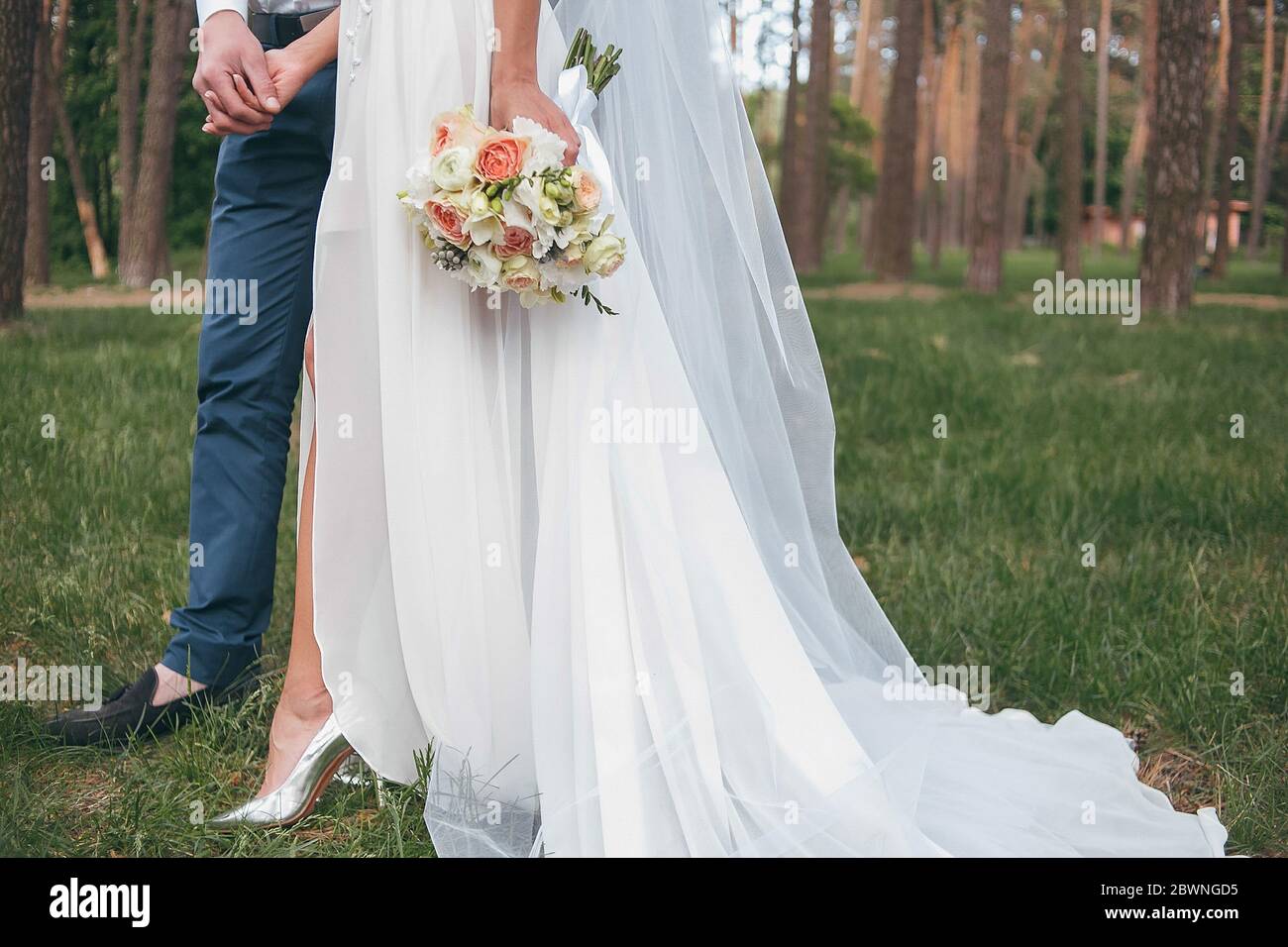 une mariée dans une belle robe avec un train tenant un bouquet de fleurs et de verdure Banque D'Images