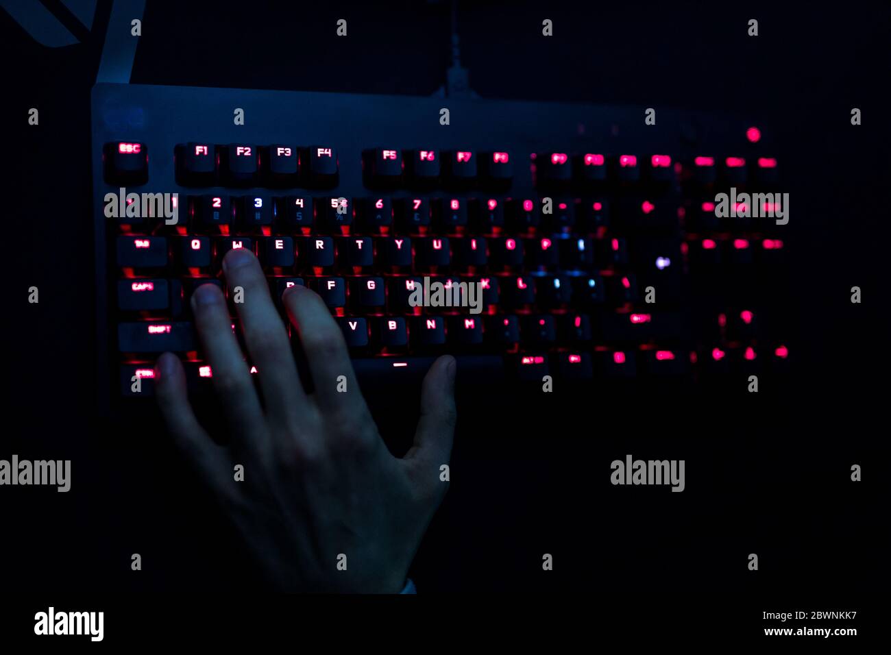 Gros plan d'un joueur passant la main sur son clavier tout en jouant à un jeu en ligne. Le clavier est rétroéclairé par des LED rouges Banque D'Images