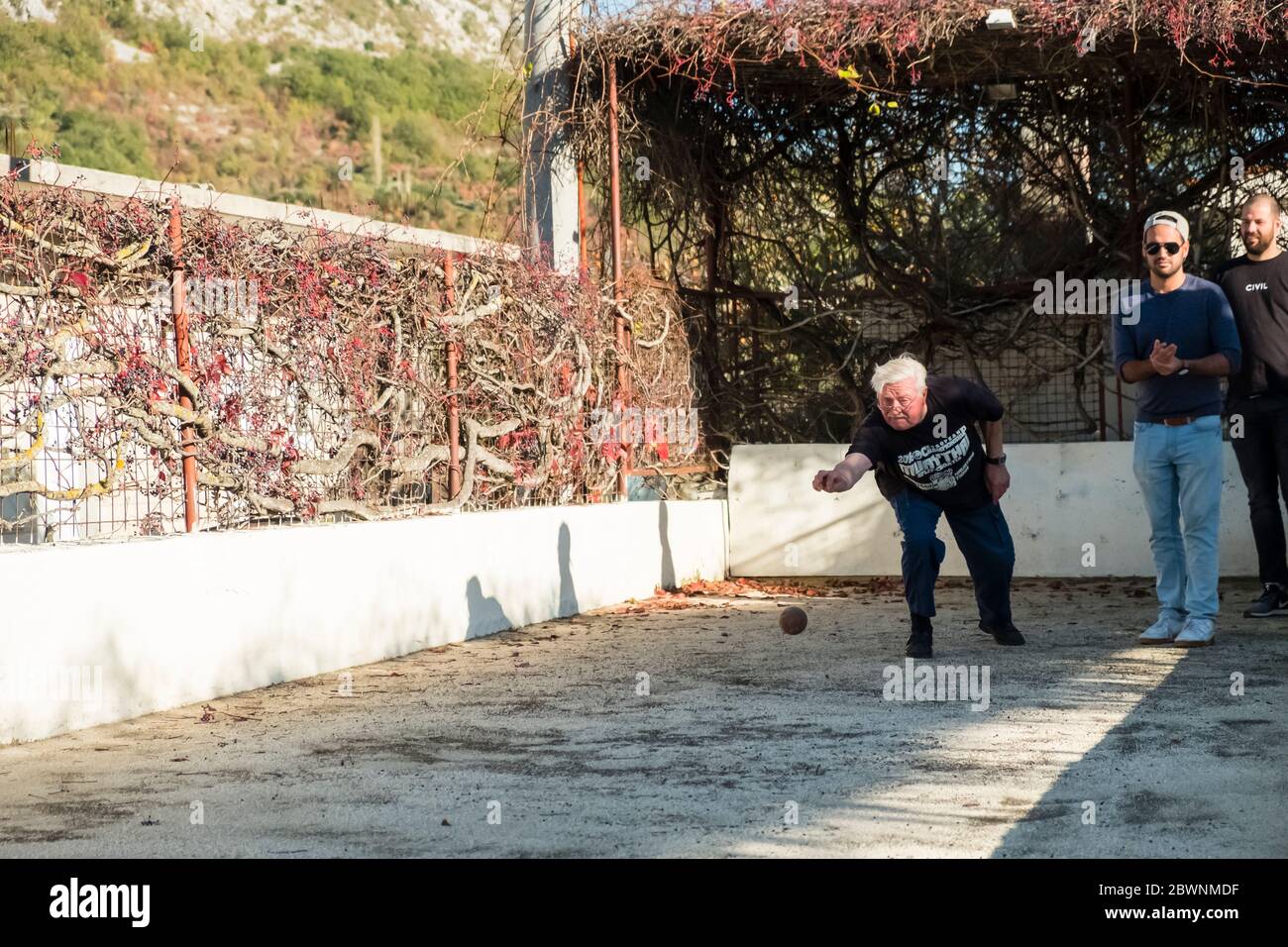 Un homme plus âgé lance une boule de bowling tandis que 2 jeunes hommes regardent, à une piste de bowling en extérieur sur pelouse à Dalmatie, Croatie Banque D'Images