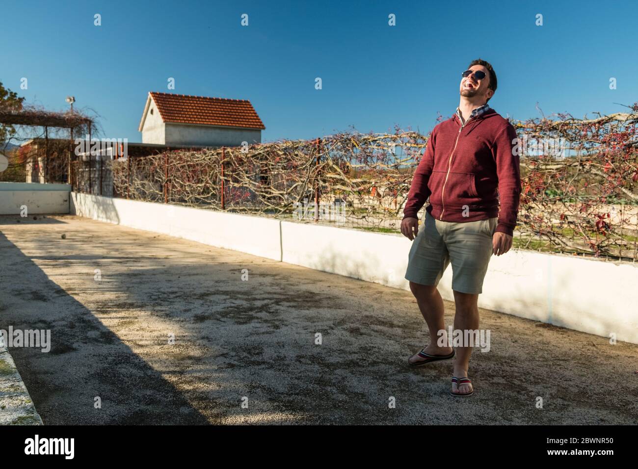 Un jeune homme portant des lunettes de soleil rit tout en faisant du bowling sur une pelouse en plein air à Dalmatie, en Croatie Banque D'Images