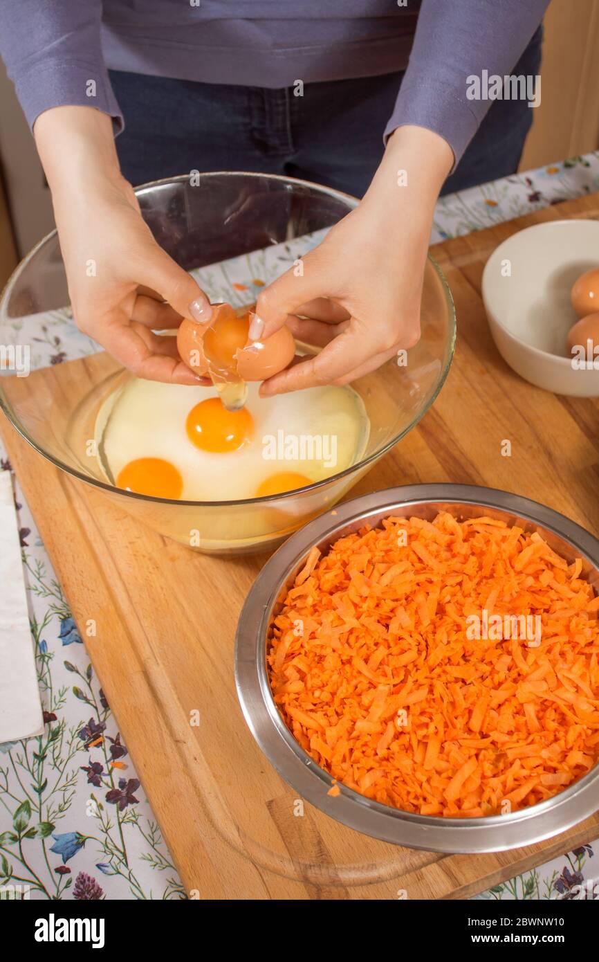 Les mains des femmes cassent l'œuf et séparent le jaune en protéine. Préparation du gâteau de carottes. Un bol en métal rempli de carottes râpées est sur le compte Banque D'Images