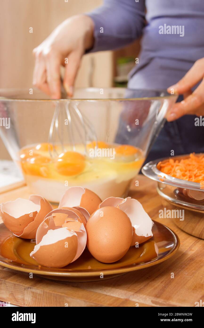 Des coquilles d'œufs de poulet se trouvent sur une soucoupe au premier plan. En arrière-plan, une femme diffuse des œufs de poulet dans un bol en verre. Préparation de la d Banque D'Images