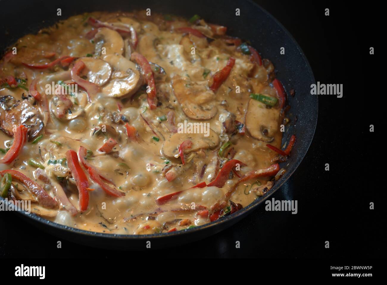 Ragoût de légumes crémeux avec poivron, champignon et oignon dans une casserole sur un poêle noir, espace de copie, foyer sélectionné, profondeur de champ étroite Banque D'Images