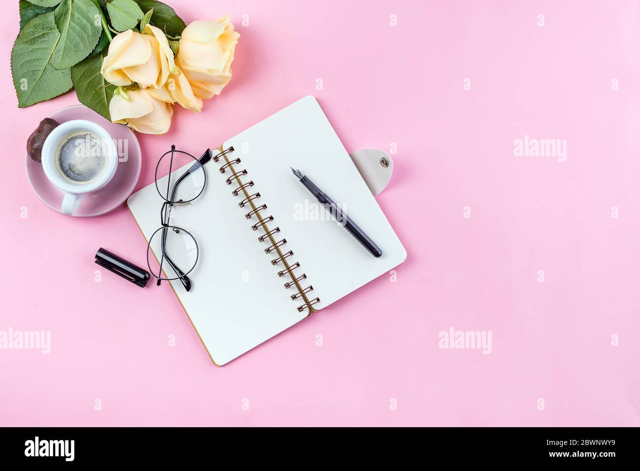 Tasse de café du matin avec verres, carnet vide, crayon et rose sur table rose vue du dessus . Femme travaillant bureau. Banque D'Images
