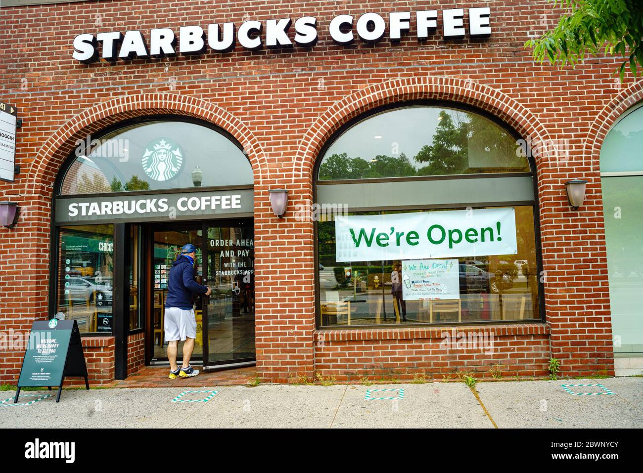 Mount Kisco, New York le 29 mai 2020 : alors que le comté de Westchester, NY, commence la première phase de réouverture après une pause en raison de la pandémie du coronavirus, Starbucks propose un service de prise de commande mobile avec un grand panneau indiquant « We're Open! » Les places à l'extérieur montrent une distance sociale de 6 pieds.UN homme entre dans le magasin. Banque D'Images