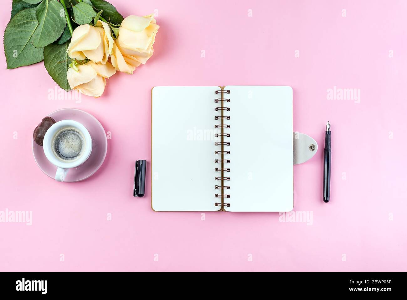 Tasse de café du matin pour le petit déjeuner, carnet vide, crayon et rose sur table rose vue du dessus . Femme travaillant bureau. Banque D'Images