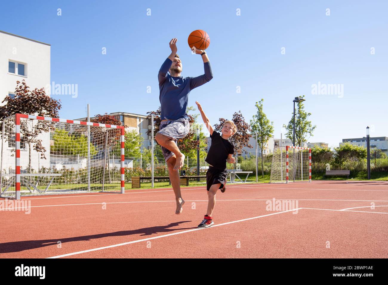 Papa et fils jouant au basket-ball pieds nus avec le ballon sur un terrain de jeu Banque D'Images
