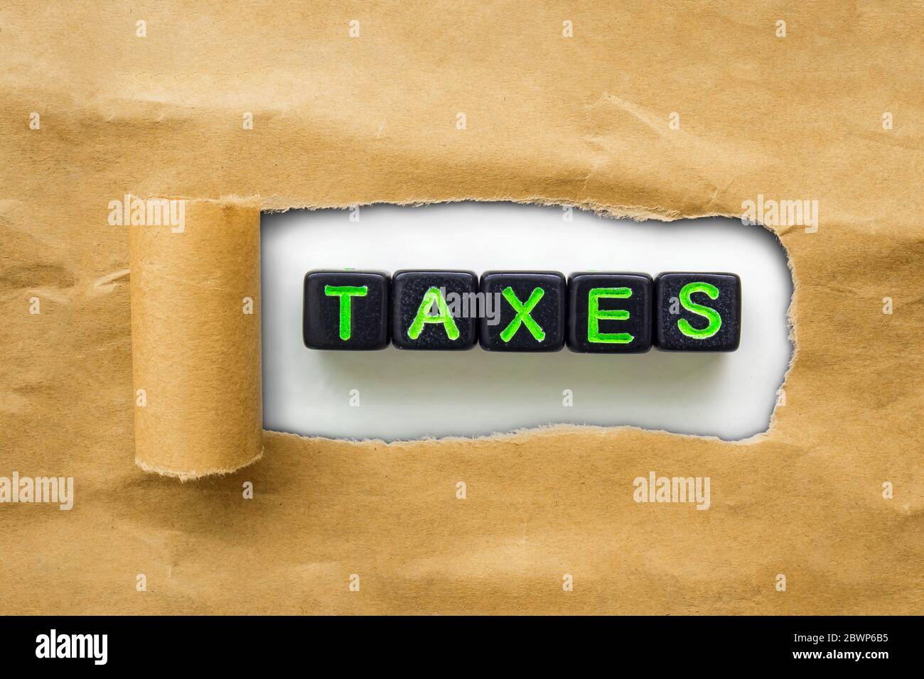 Papier kraft brun déchiré pour révéler des cubes noirs avec le mot TAXS. Concept de saison d'imposition Banque D'Images