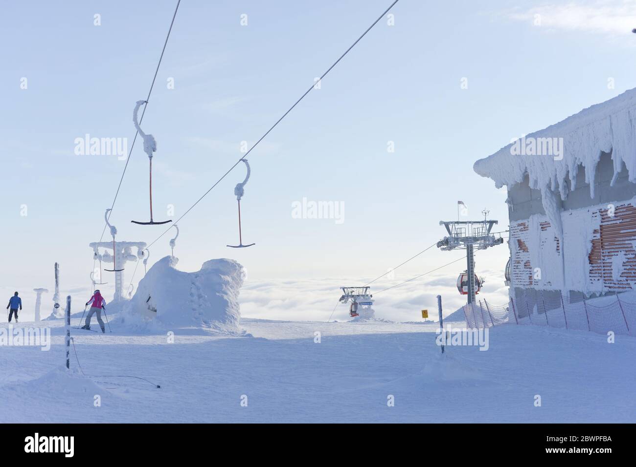 deux skieurs descendent une piste en débarqué des remontées mécaniques qui s'élèvent au-dessus des nuages dans le ciel bleu pâle. Très froid et enneigé. Banque D'Images