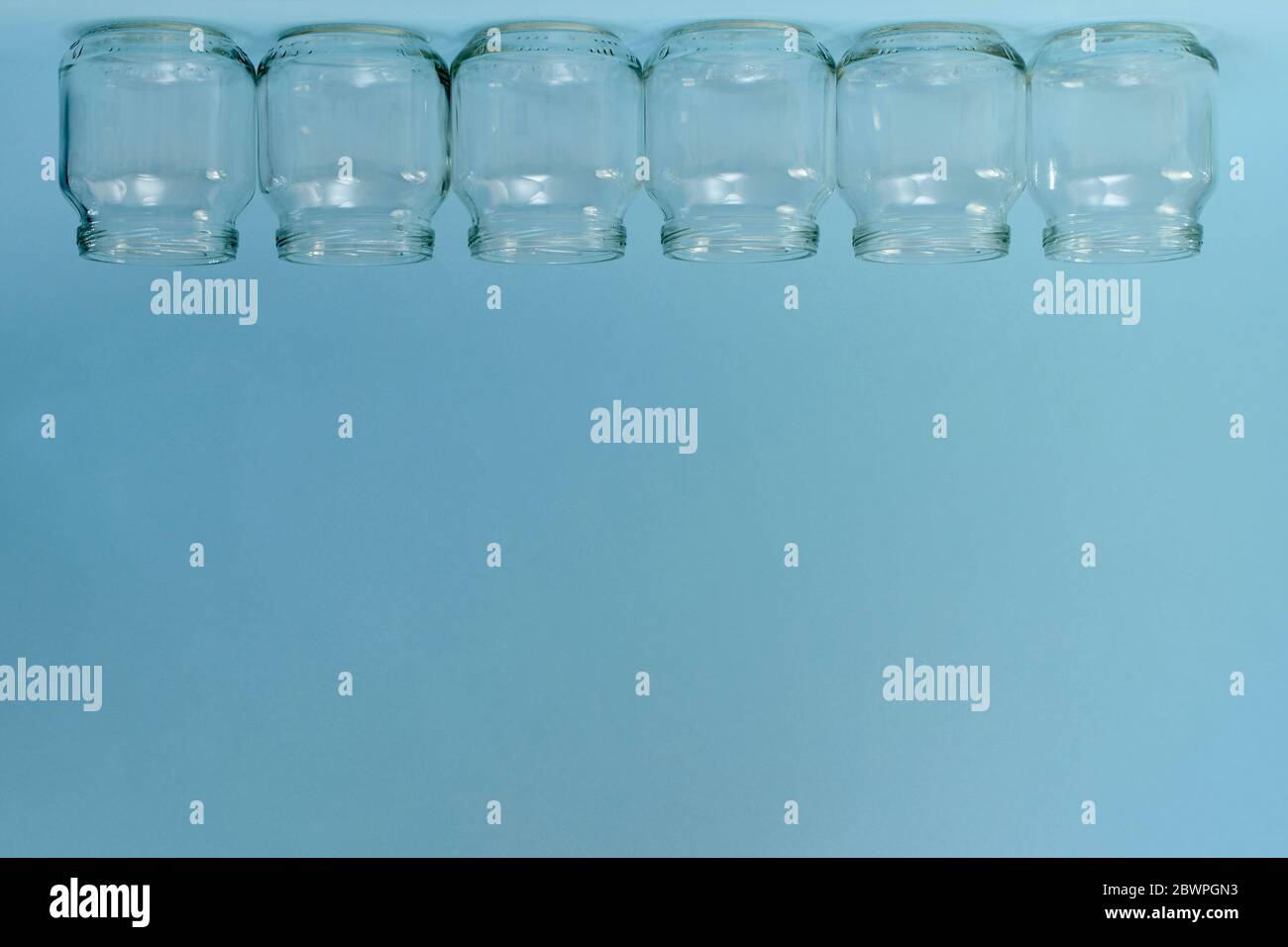 Une rangée horizontale de six pots transparents inversés en haut du cadre sur un fond bleu libre. Banque D'Images